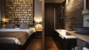 Une chambre à coucher moderne avec un mur en pierre, un grand lit, des lampes de chevet et une baignoire intégrée.