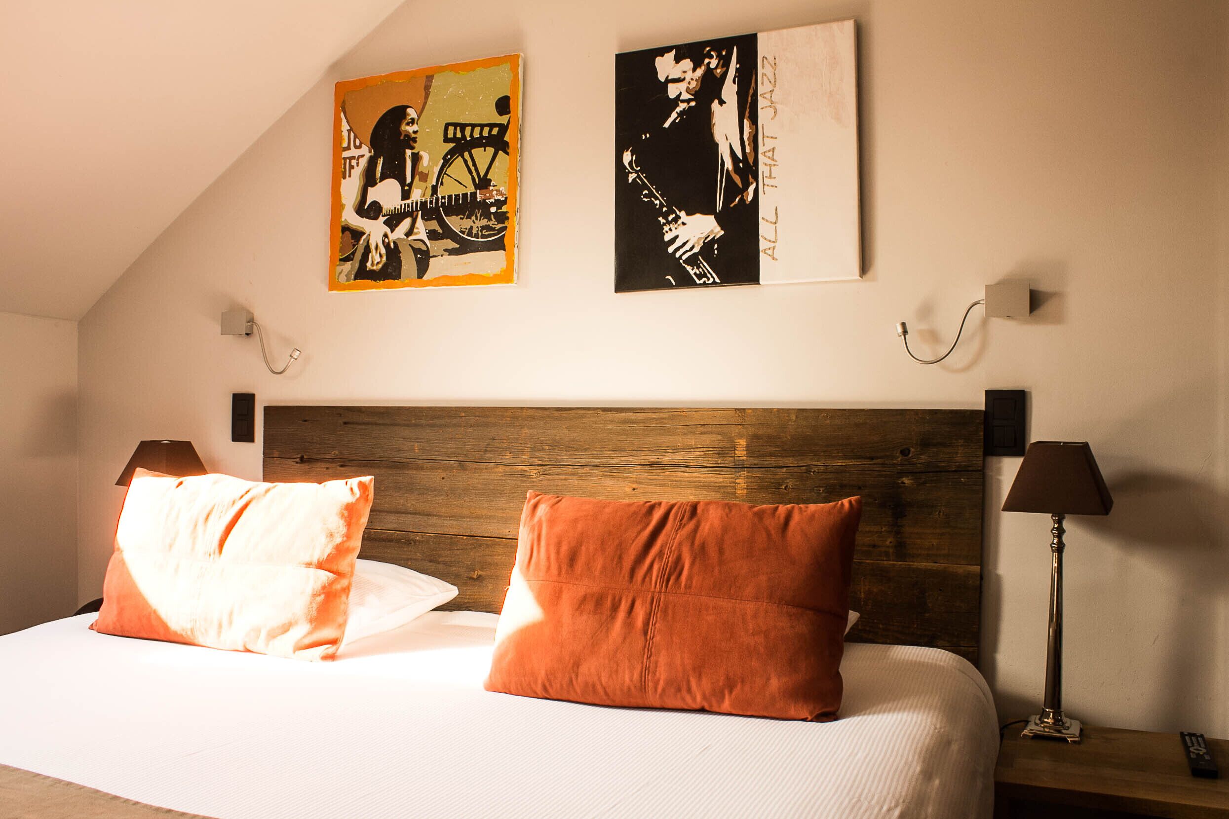Une chambre à coucher avec une tête de lit en bois, deux oreillers, une table de chevet avec une lampe et deux tableaux encadrés accrochés au mur.