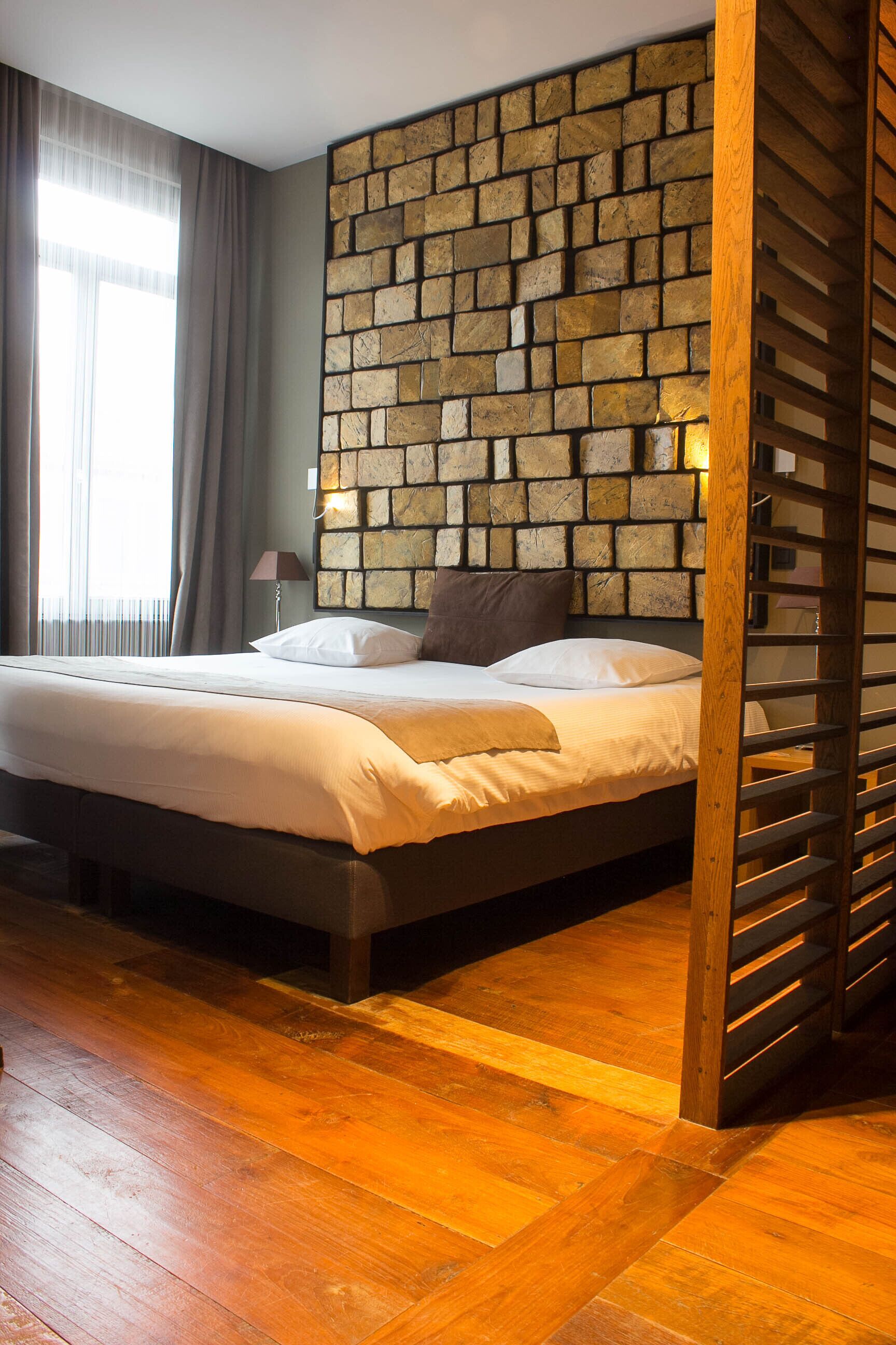 A bedroom with a bed, wooden floor, and a stone wall.
