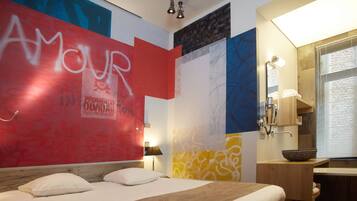 A hotel room with a bed, a bedside table, a mirror, and a bathroom with a sink and a bowl on the counter.