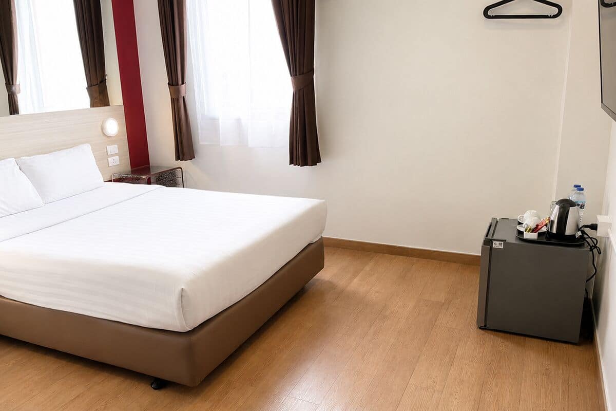 A hotel room with a bed, a small desk with a kettle, and a water bottle.