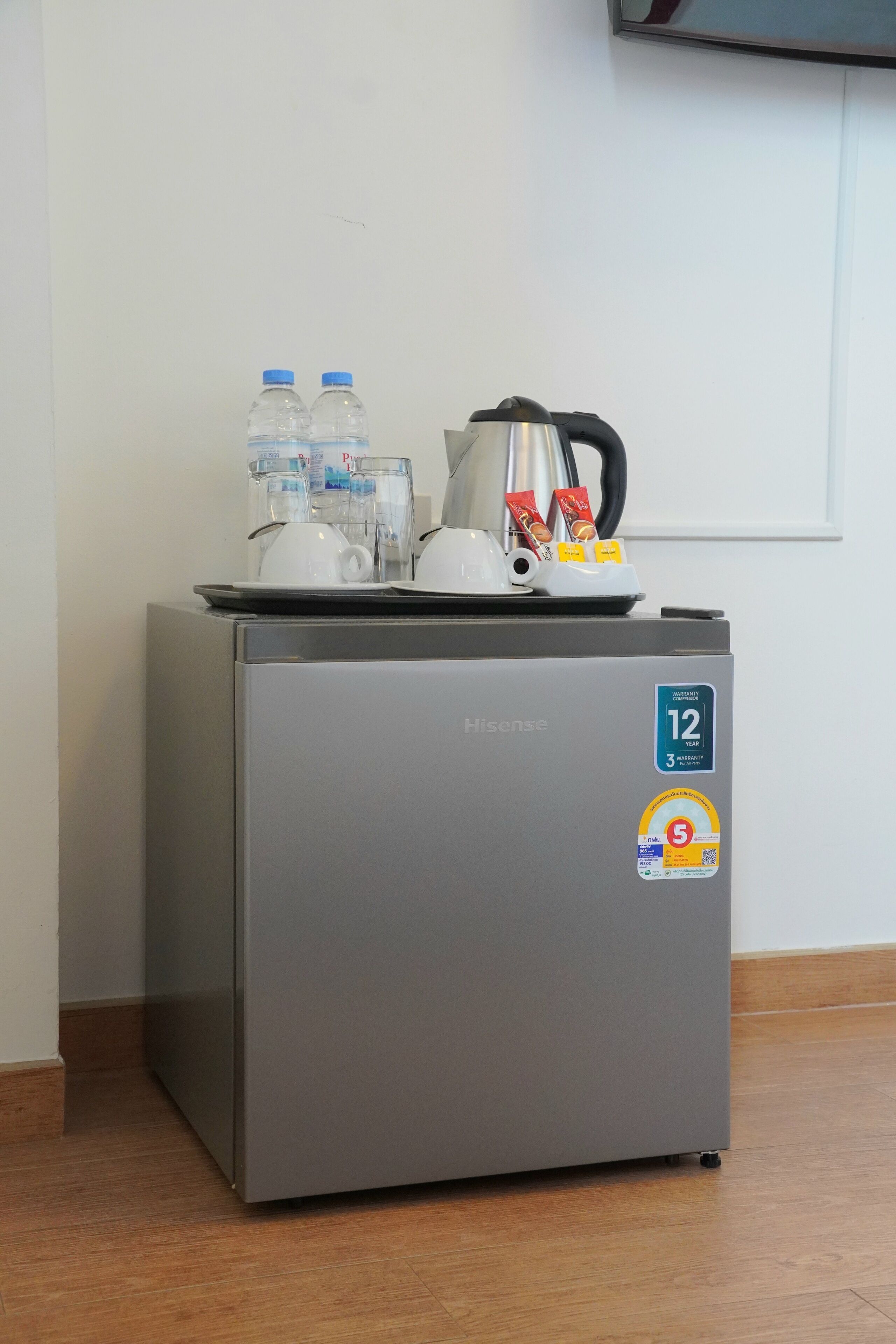 A compact refrigerator with a warranty sticker, a kettle, and some water bottles on top.