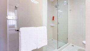 A modern bathroom with a glass shower enclosure, a white towel on the door, and a toilet visible in the background.