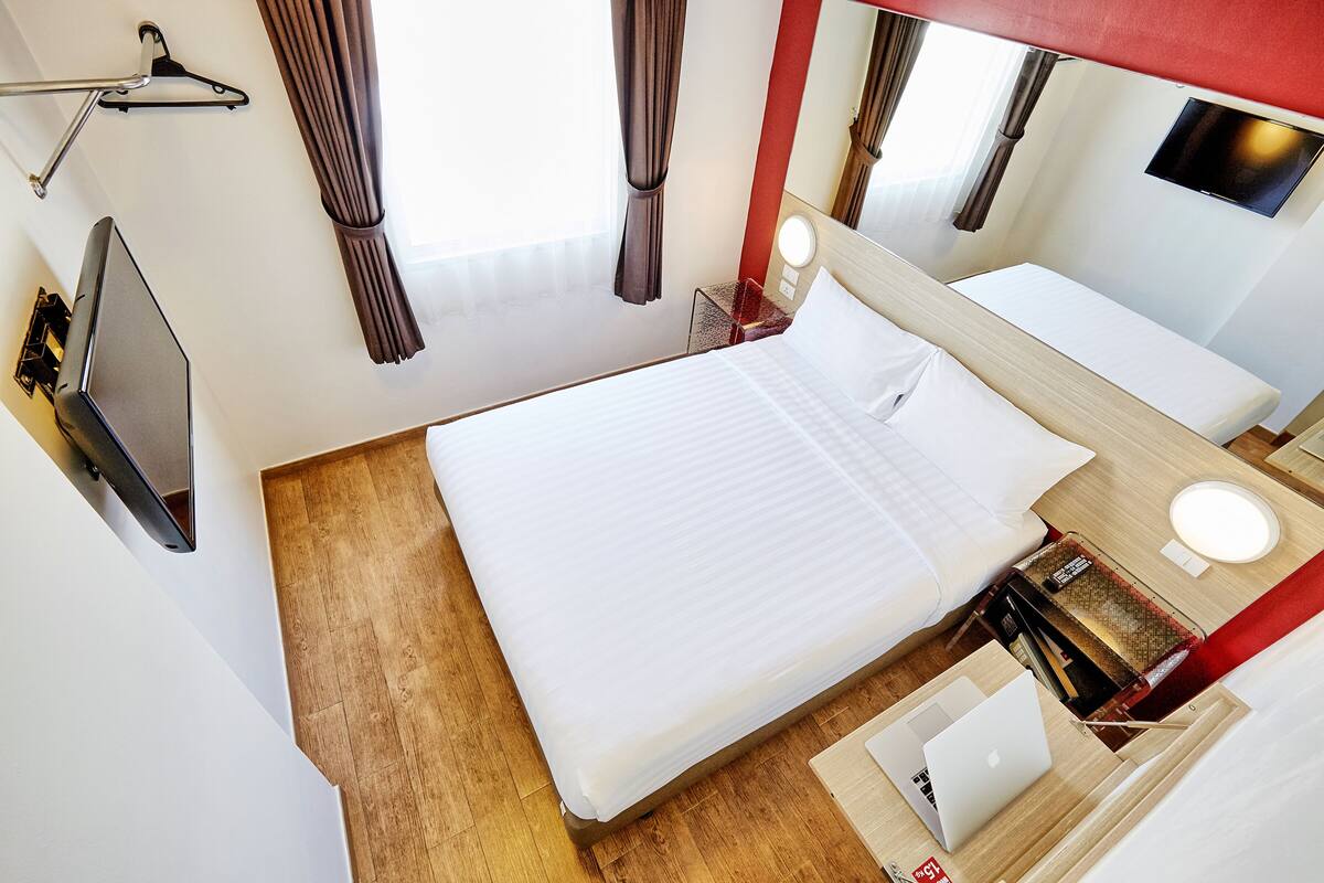 A hotel room with a bed, a desk with a laptop, a TV, and a mirror.