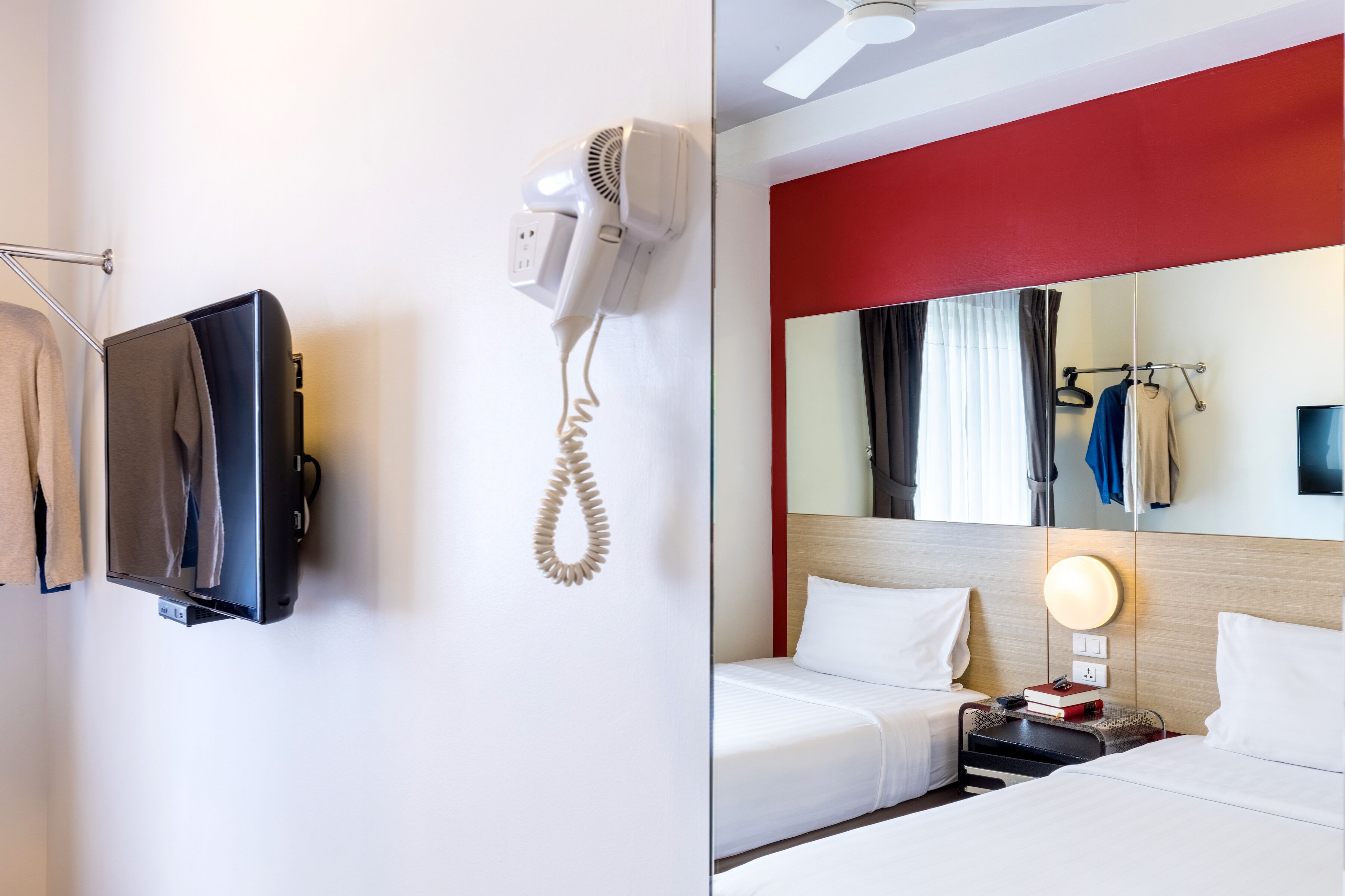 Ein Hotelzimmer mit Flachbildfernseher an der Wand, Fön, Spiegel mit Beleuchtung und einem Bett mit weißer Bettwäsche.