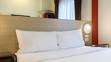 A hotel room with a wooden headboard, white bedding, a bedside table, and a coat rack with clothes.