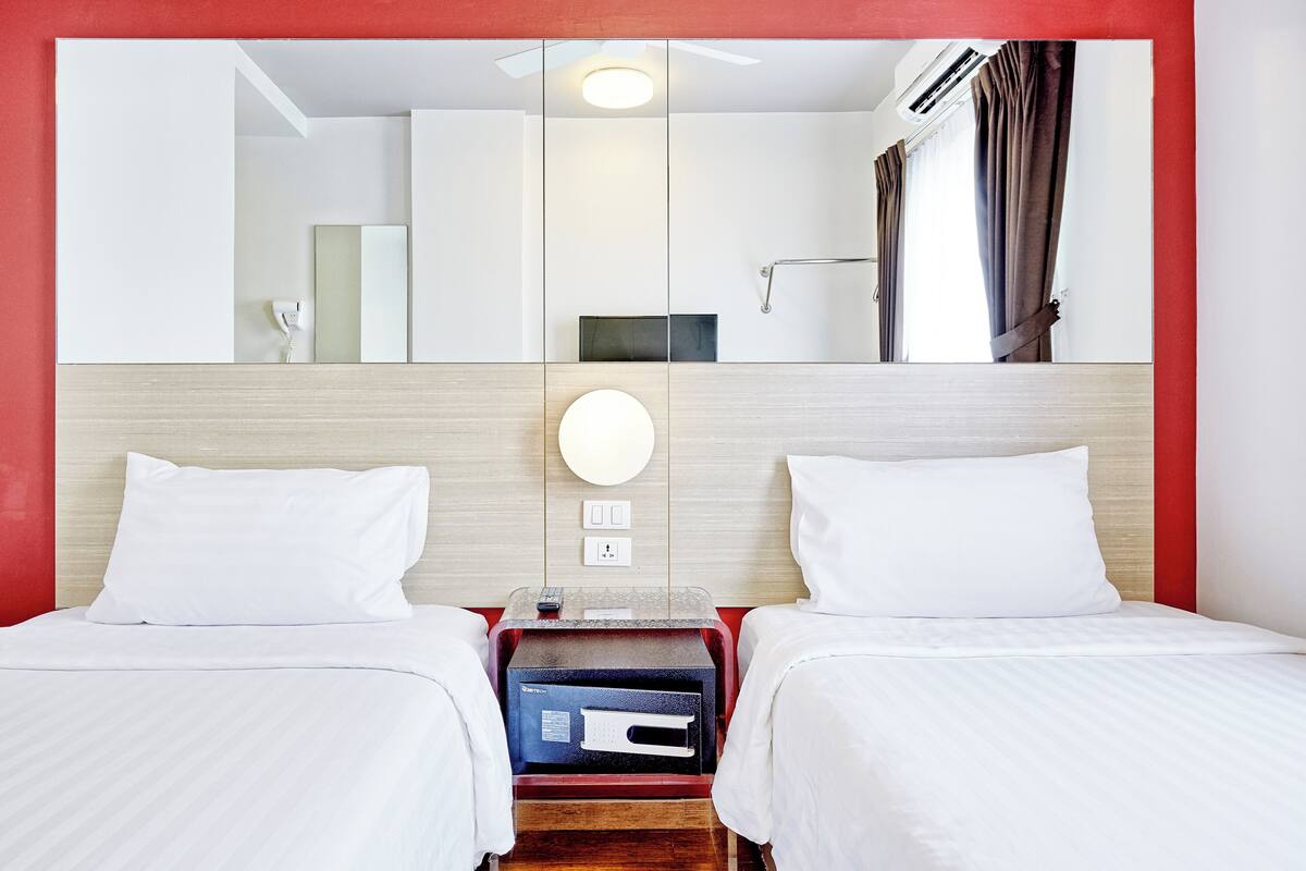 A hotel room with two beds, a large mirror, a ceiling fan, an air conditioning unit, and a red accent wall.