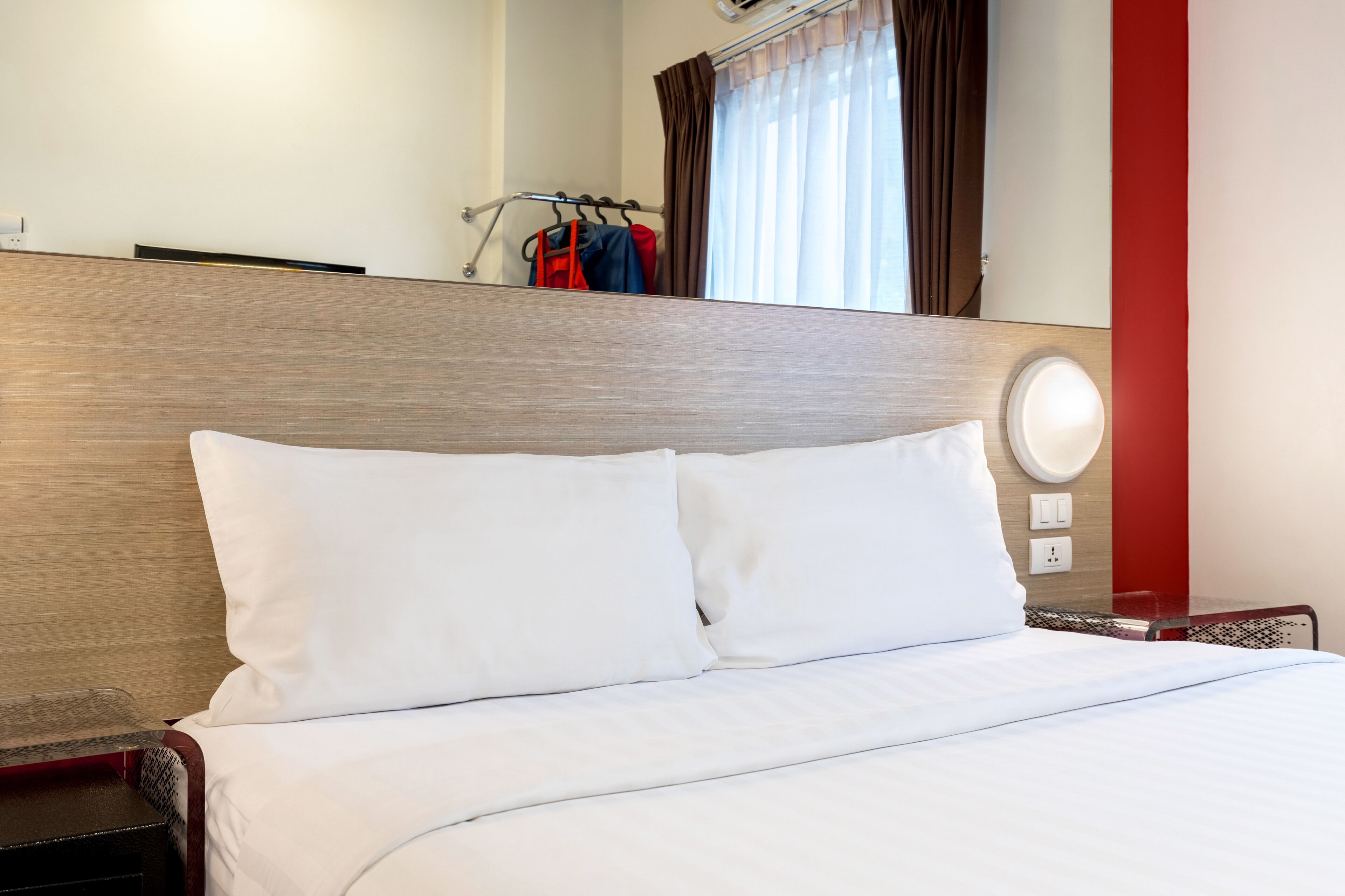 A hotel room with a wooden headboard, a bed with white bedding, a bedside table, and a wall-mounted light fixture.