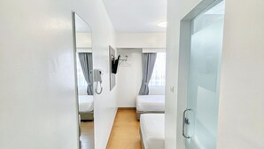 Een hotelkamer met een houten vloer, twee bedden, een spiegel, een telefoon en een raam met gordijnen.