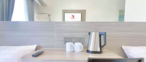 Ein Hotelzimmer mit Bett, Schreibtisch, Kaffeemaschine, Fernbedienung und Fernseher.