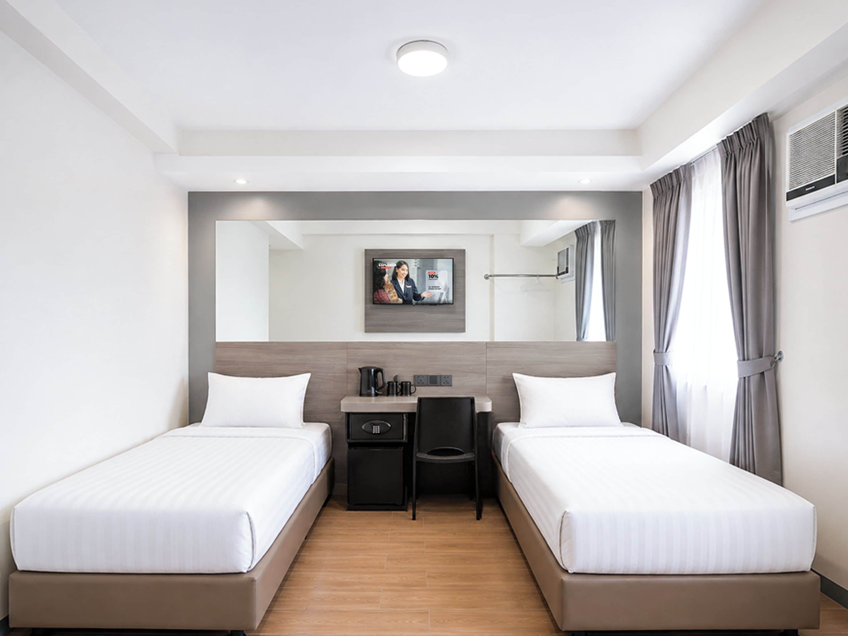 A hotel room with two single beds, a desk, a chair, a coffee maker, and a television mounted on the wall.