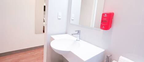 Une salle de bain moderne avec un lavabo blanc, un miroir et un distributeur de savon rouge.