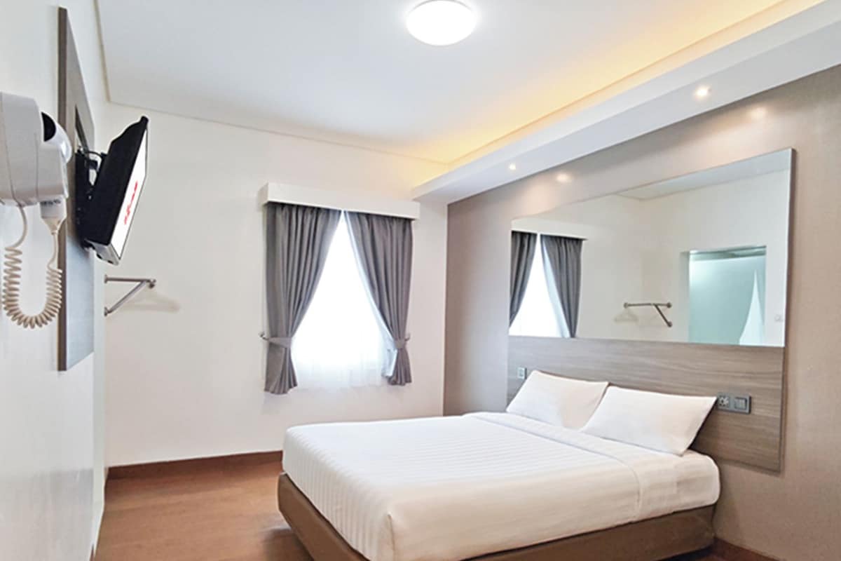 A hotel room with a bed, a mounted TV, and a large mirror.