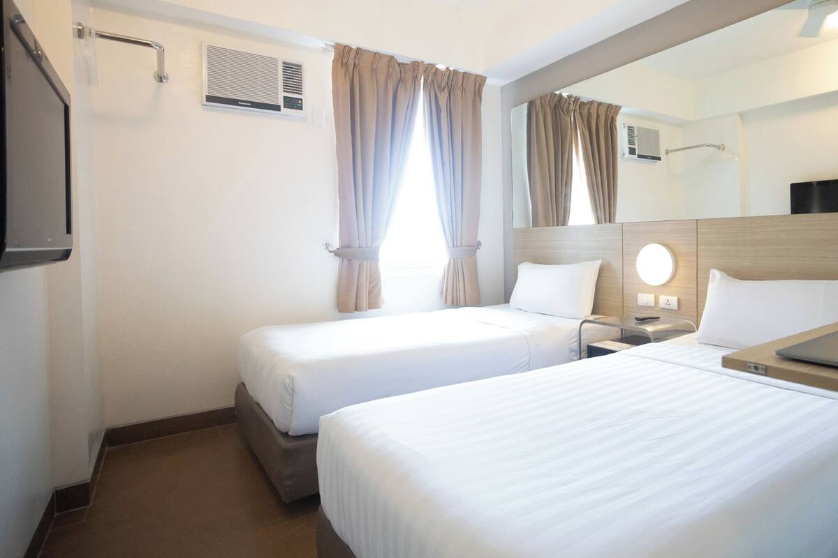 A hotel room with two beds, a desk with a laptop, a mirror, and a TV.