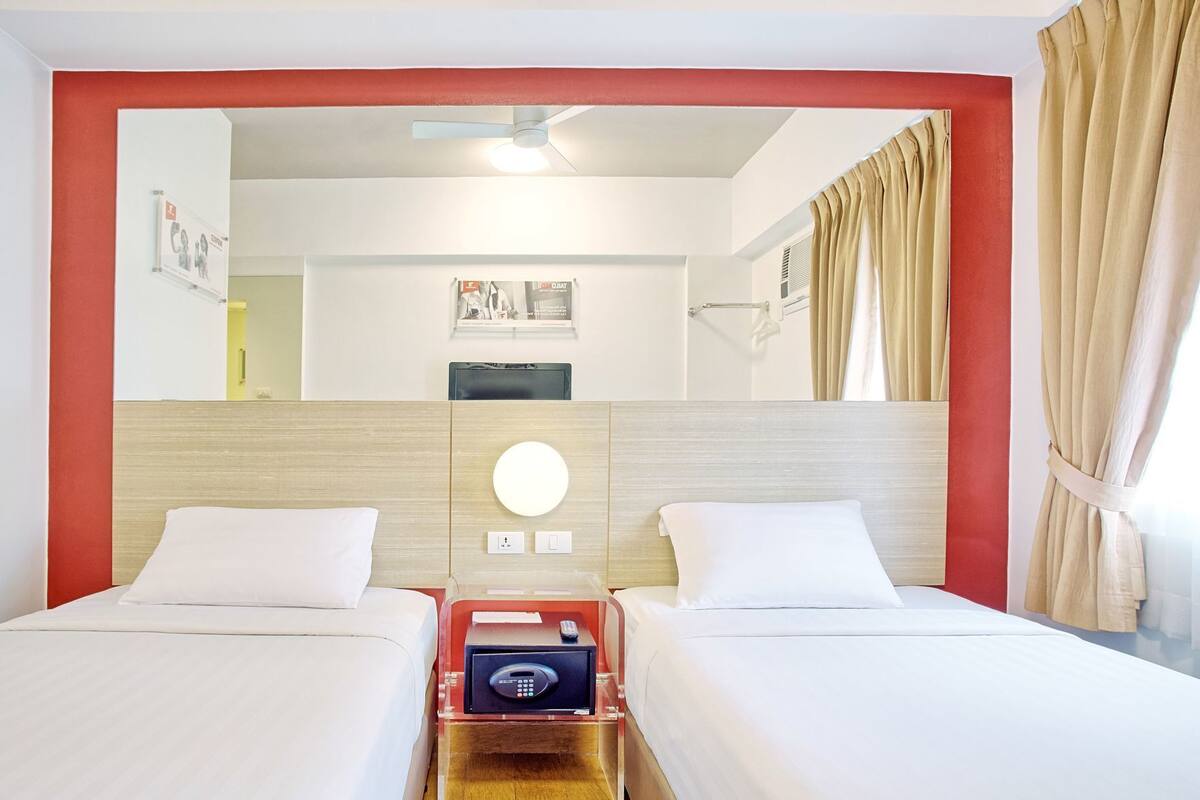 A hotel room with two beds, a minibar, a round mirror, and a ceiling fan.