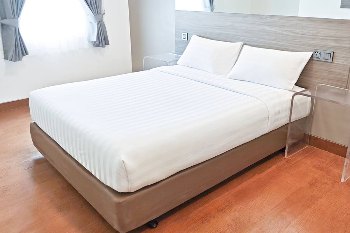 A modern hotel room with a single bed, a nightstand, a power outlet, and a window with curtains.