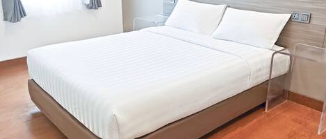 Una habitación de hotel moderna con una cama individual, una mesita de noche, un enchufe y una ventana con cortinas.