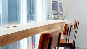 Een houten tafel met een laptop en twee monitoren op een standaard, geplaatst bij een raam met jaloezieën.