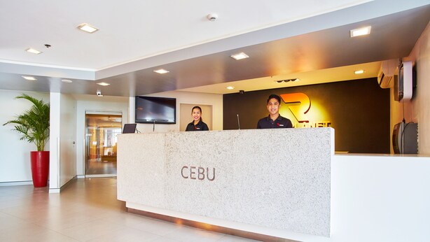 Een receptiebalie met de naam 'CEBU' duidelijk zichtbaar, twee medewerkers achter de balie en een groot scherm erboven.