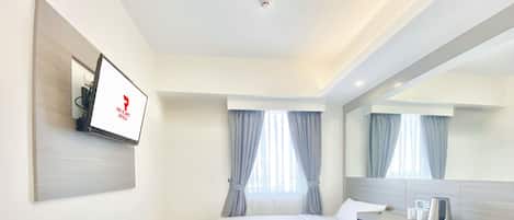 A hotel room with two beds, a TV mounted on the wall, a bedside table with a kettle, and a large mirror.