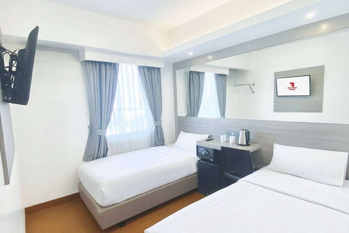 A hotel room with two beds, a desk, a chair, a TV, and a window with curtains.