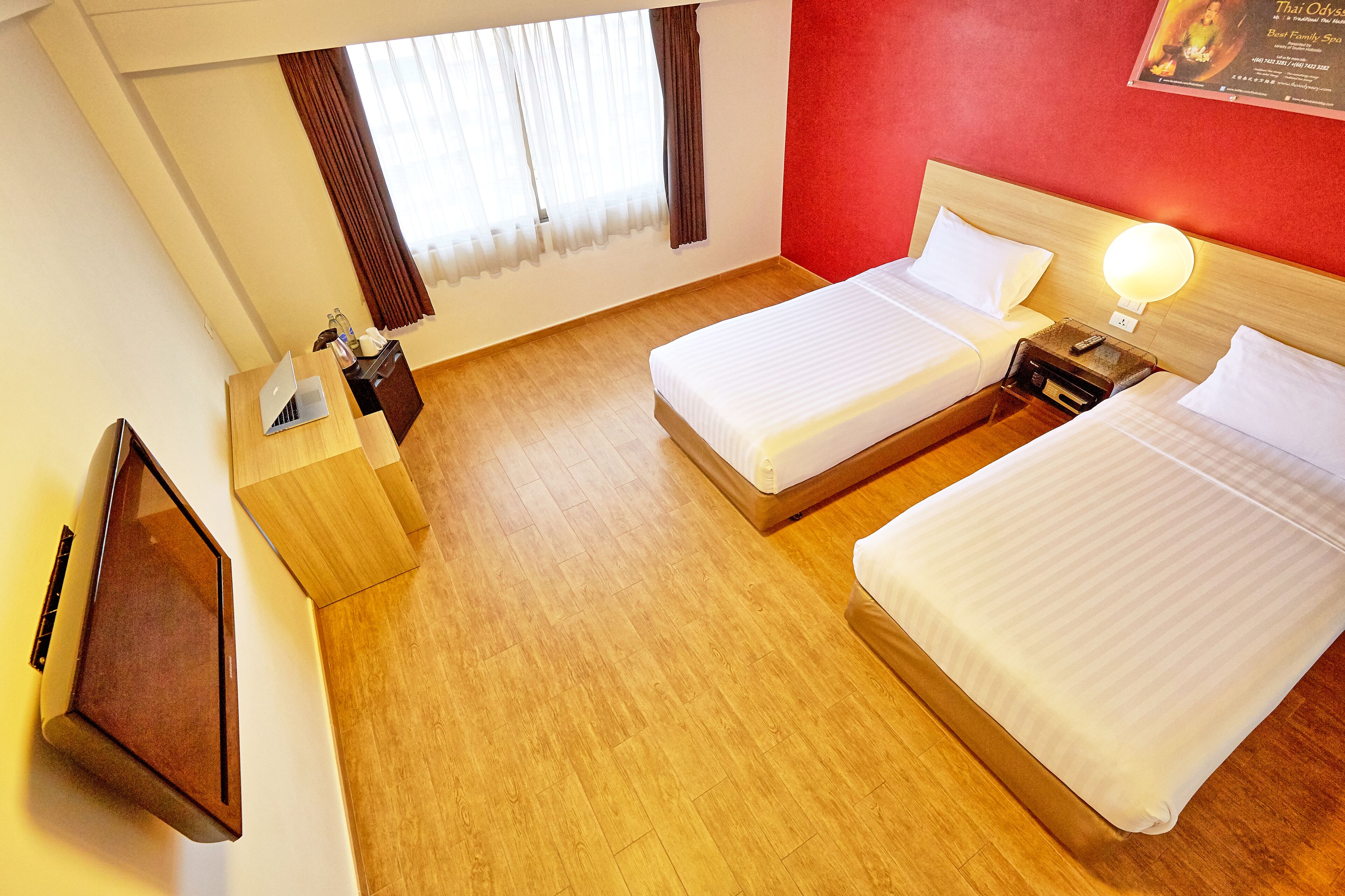 A hotel room with two beds, a wooden desk, a laptop, and a TV.