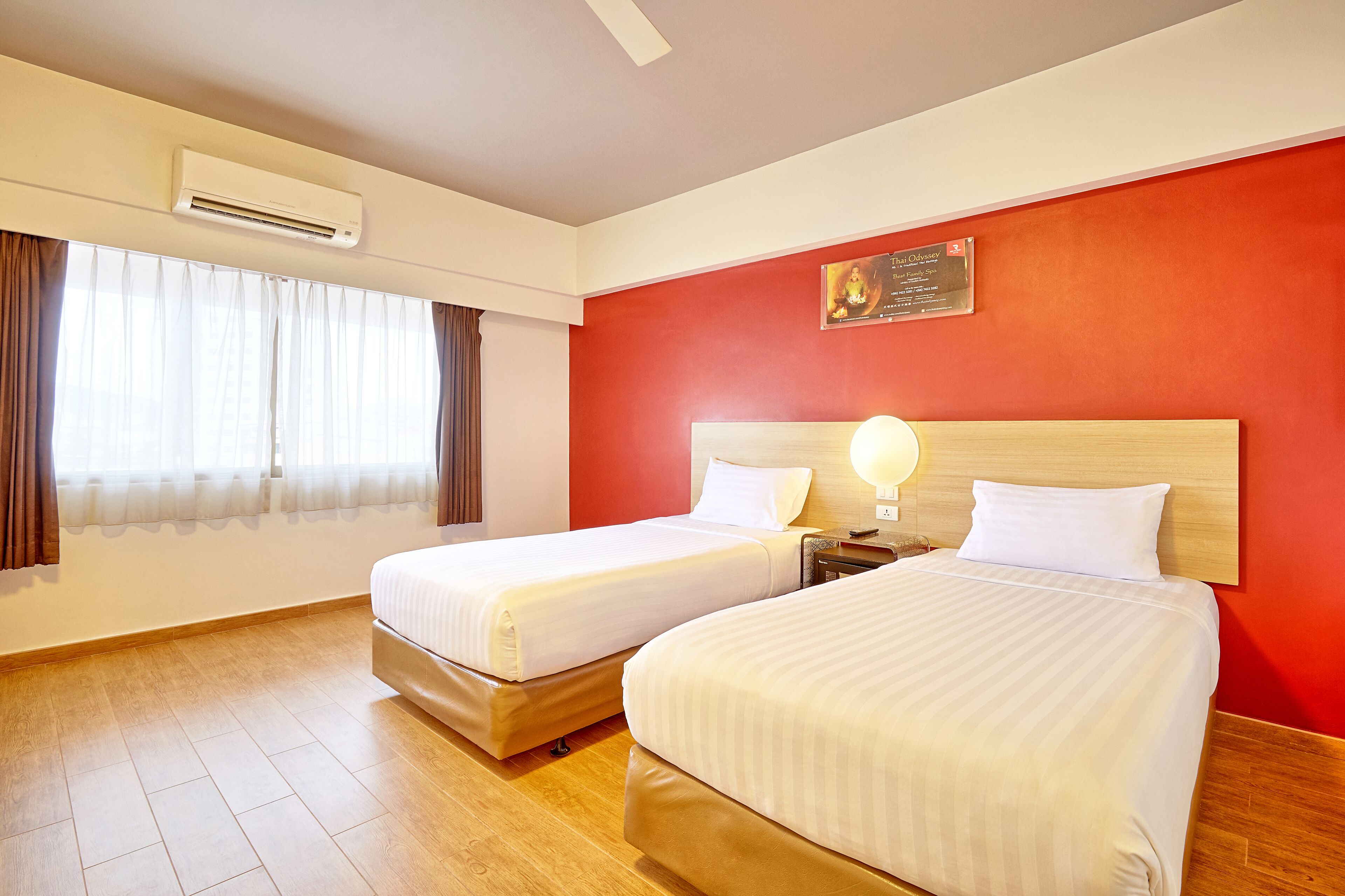 Une chambre d’hôtel avec deux lits, un mur d’accent rouge, un appareil de climatisation et une fenêtre avec des rideaux.