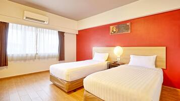 Une chambre d’hôtel avec deux lits, un mur d’accent rouge, un appareil de climatisation et une fenêtre avec des rideaux.