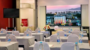 A conference room with tables, chairs, water bottles, a TV, and a large screen displaying a cityscape. - Easy Planet Hat Yai (Hat Yai)