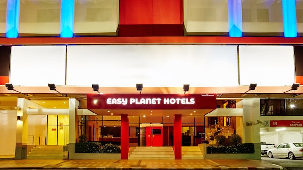 The exterior of the Easy Planet Hotels with a red facade, glass entrance, and visible parking area. - Easy Planet Hat Yai (Hat Yai)
