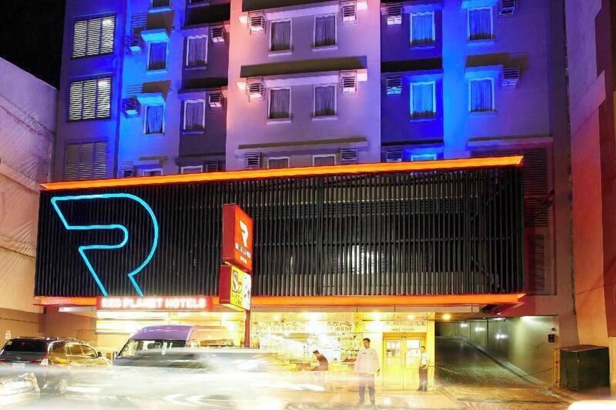 Un hotel amb un rètol de neó, una zona d'aparcament i una façana d'edifici amb diverses finestres.