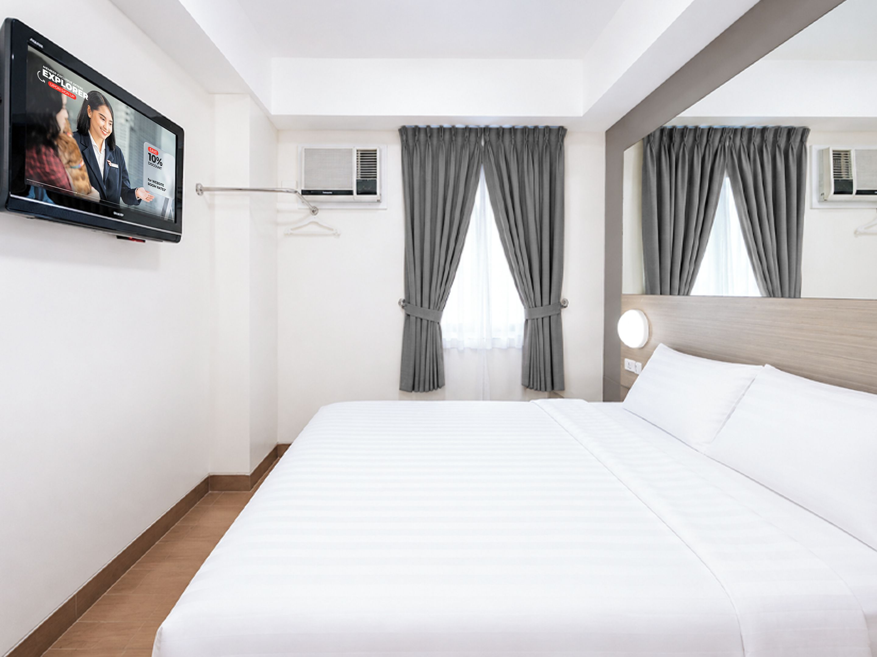 A hotel room with a bed, a television mounted on the wall, and a window with curtains.