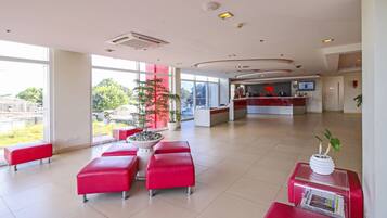 A spacious lobby with red seating, a reception desk, and large windows offering a view of the outdoors.