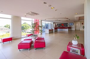 A spacious lobby with red seating, a reception desk, and large windows offering a view of the outdoors.