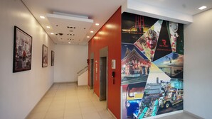 Un pasillo de hotel con una pared de acento rojo, fotografías enmarcadas a la izquierda y un cartel grande con diversas escenas de viajes a la derecha.