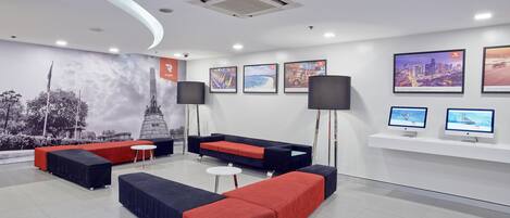 A modern lobby with seating areas, a large mural, and multiple screens.