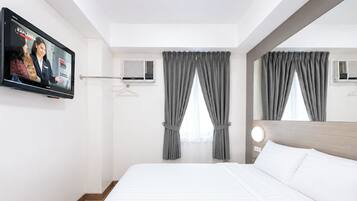 Habitación de hotel con cama, televisor montado en la pared y ventana con cortinas.