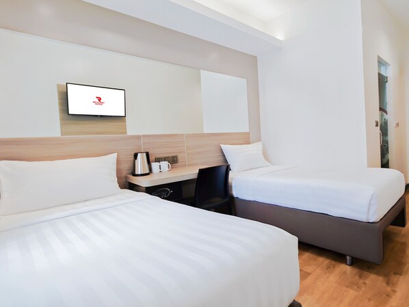 Habitación de hotel con dos camas, un escritorio, una cafetera y un televisor en la pared.