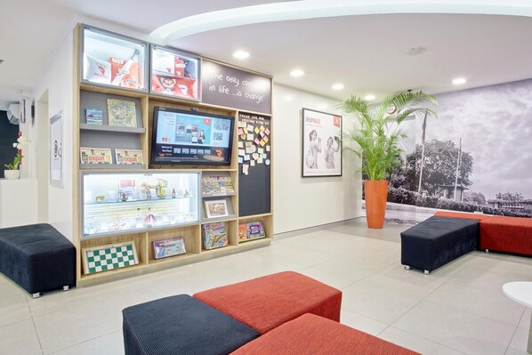 Zona de recepción con una pantalla digital, una pared con libros infantiles y una cita motivacional, y áreas de descanso.