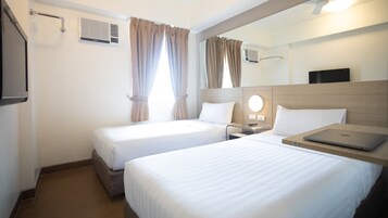 A hotel room with two beds, a desk with a laptop, a mirror, and a TV.