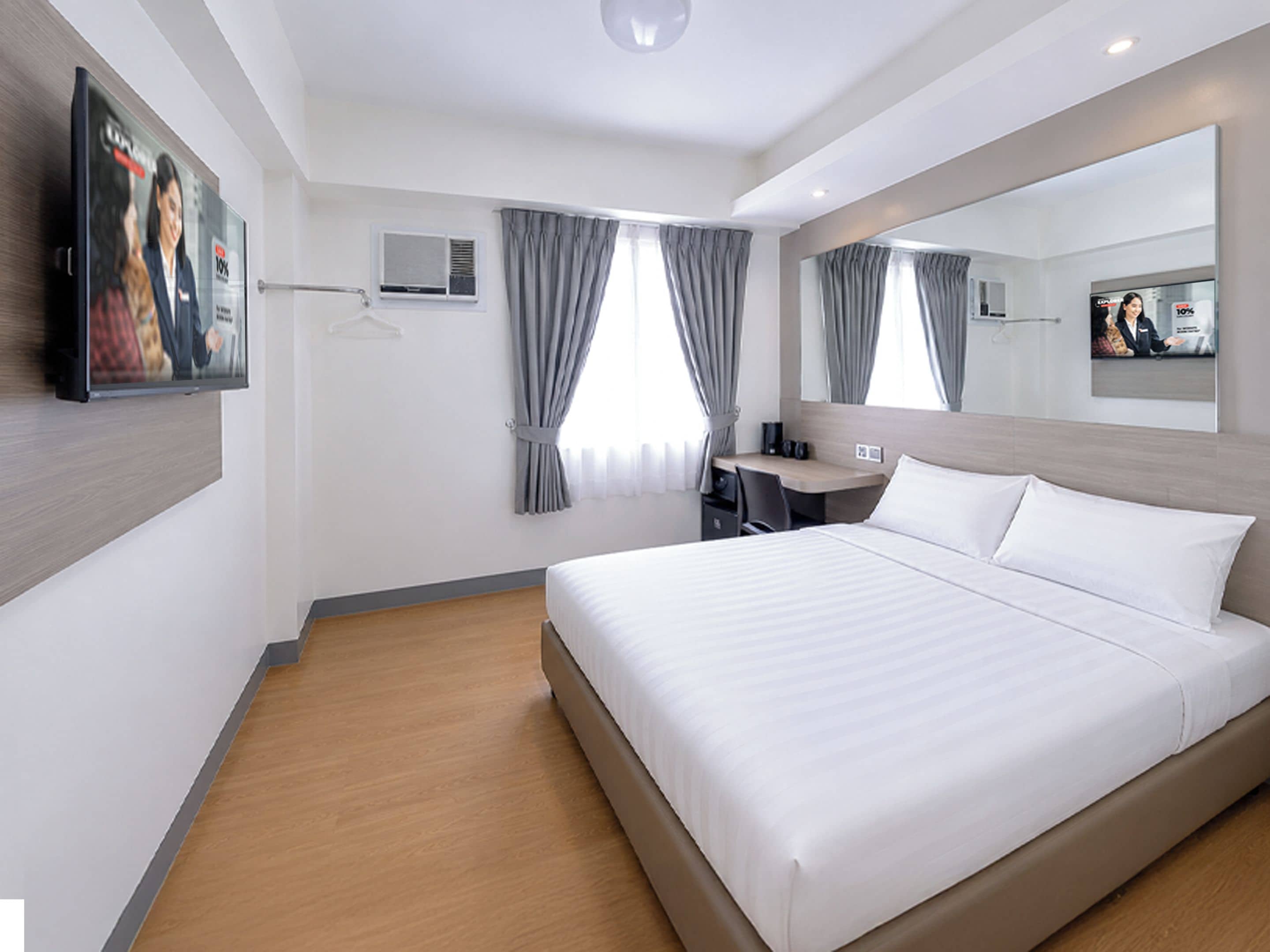 A modern hotel room with a large bed, a desk, a chair, a flat-screen TV, and a mirror.