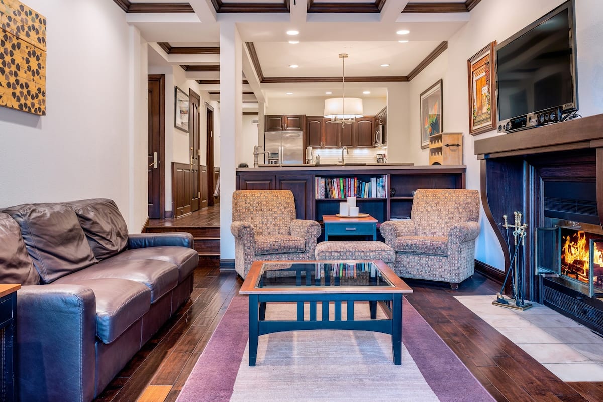 A modern living room with a leather sofa, patterned armchairs, a glass coffee table, and a fireplace.