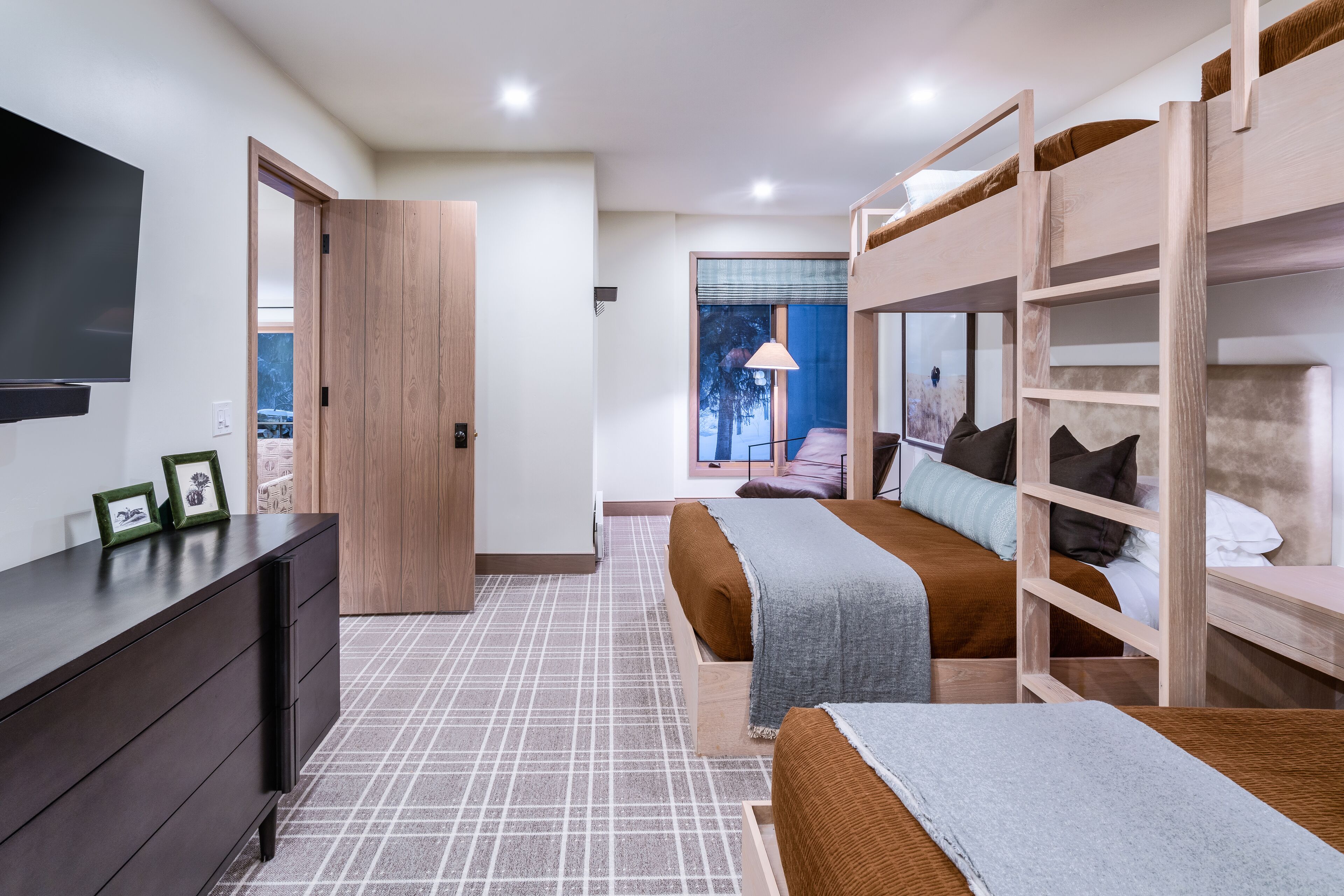 A modern bedroom with a large bed, a TV, a dresser, and a view of the outdoors.