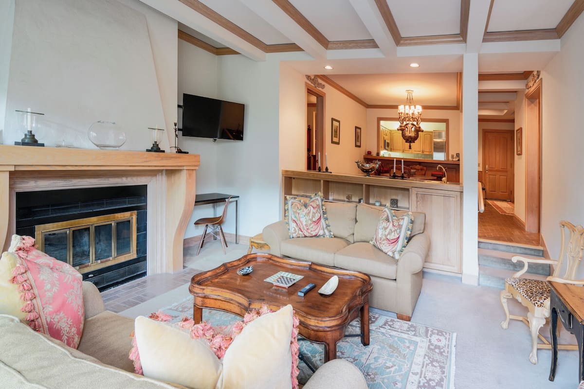 A spacious living room with a fireplace, a sofa set, a coffee table, and a television mounted on the wall.
