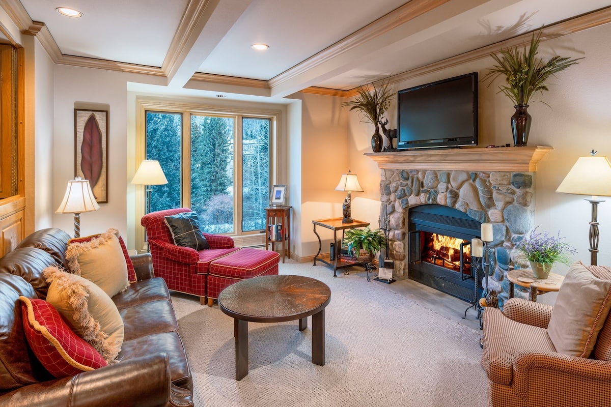 A cozy living room with a stone fireplace, leather sofas, and a television mounted above it.