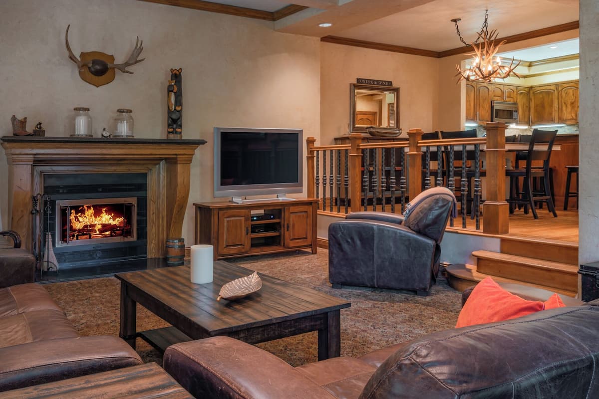 A cozy living room with a fireplace, leather sofas, a TV, and a staircase leading to a dining area.