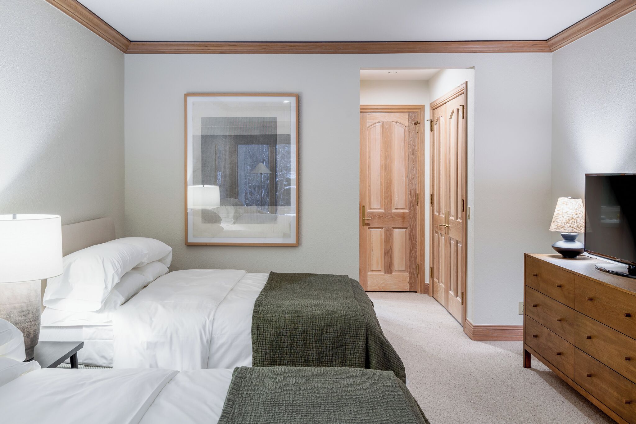 Een hotelkamer met twee bedden, een televisie, een dressoir en een ingelijst schilderij aan de muur.