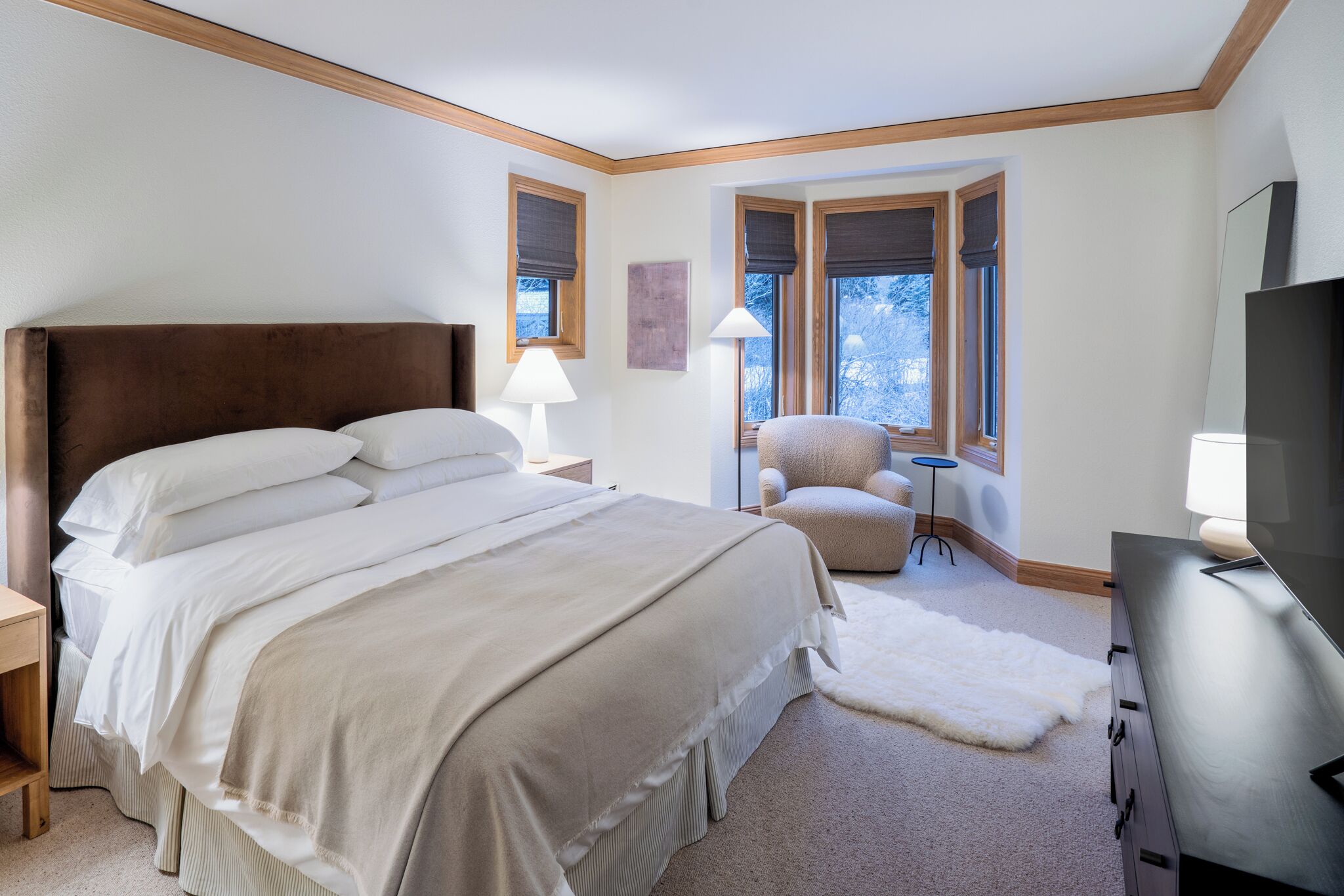 Une chambre avec un grand lit, une chaise, une télévision et une fenêtre donnant sur des arbres.