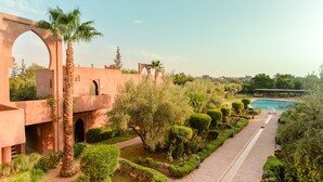 Un jardín ajardinado con piscina, palmeras y un edificio con arcos.