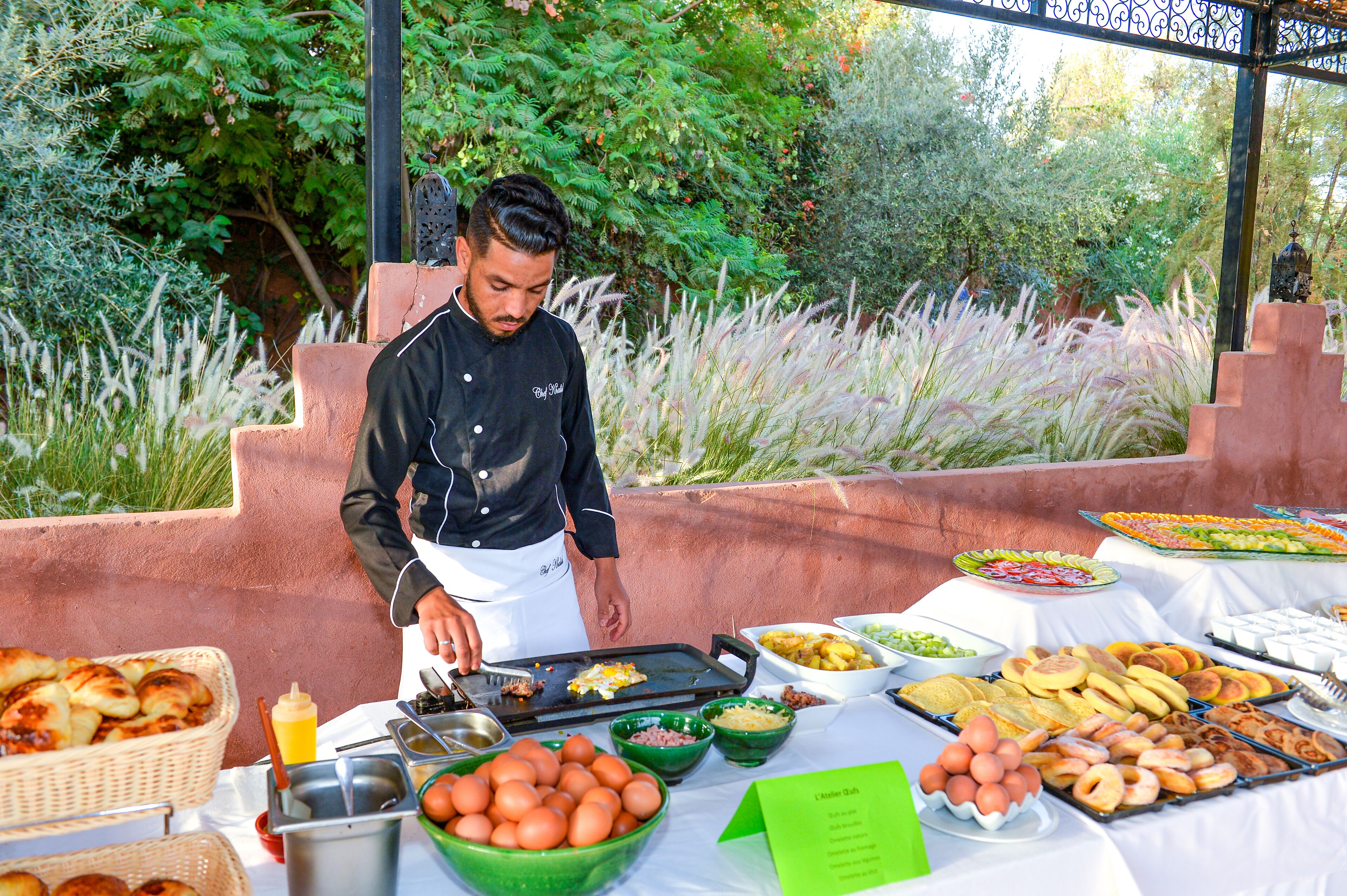 A chef preparing food outdoors with a buffet table full of various dishes.